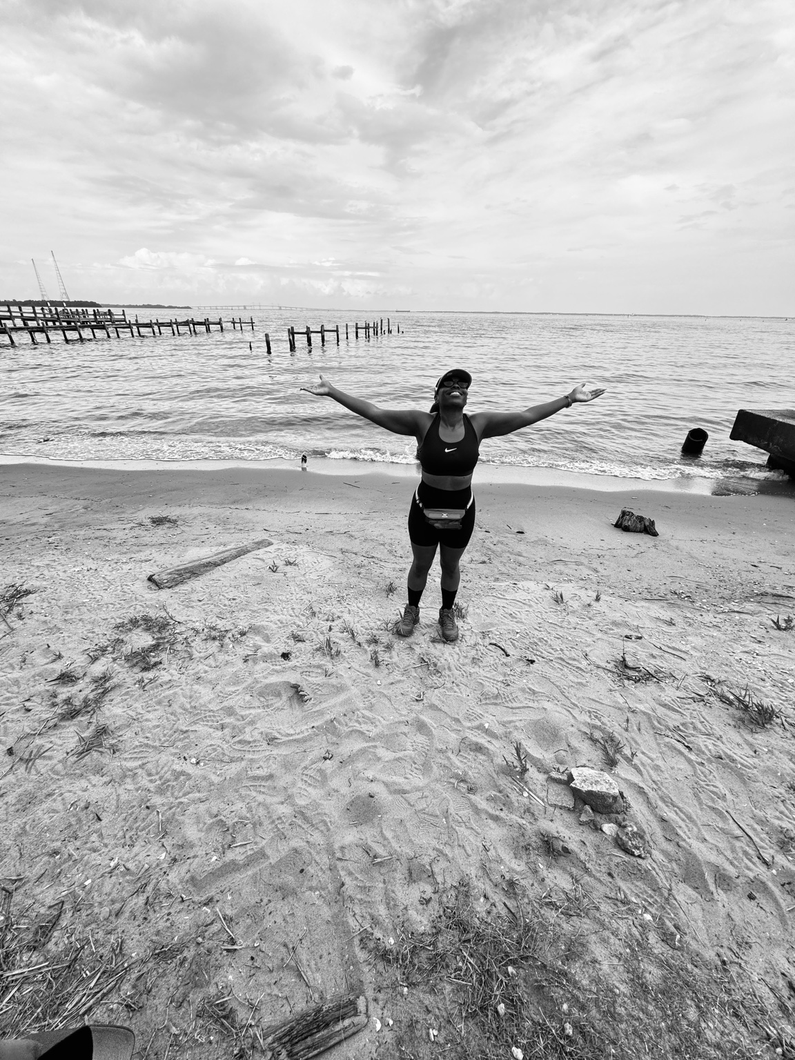 Denise Taylor standing on a beach with arms open toward the water, reflecting peace and release.