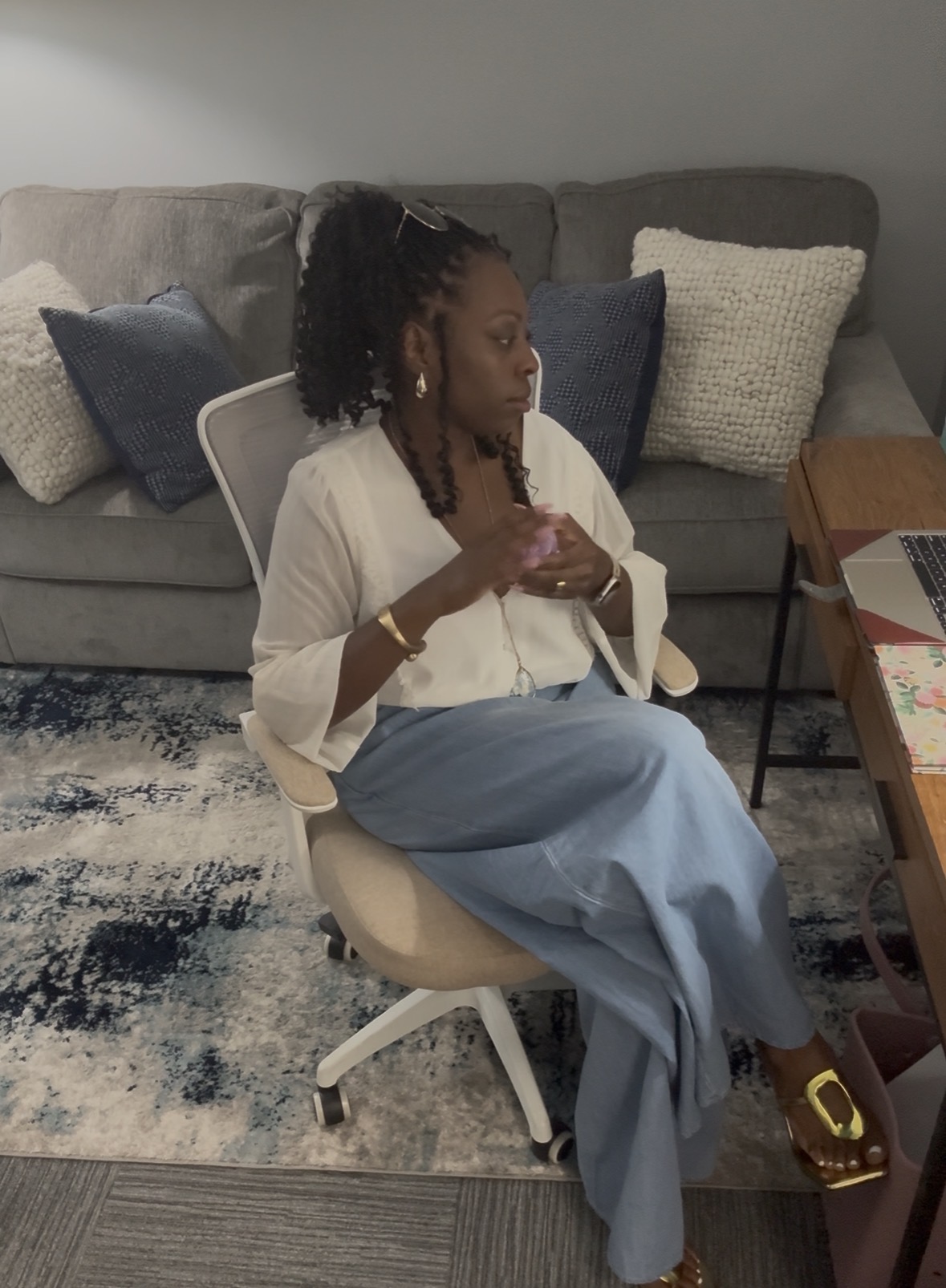 Denise Taylor sitting calmly in her therapy office beside her laptop and soft office decor.